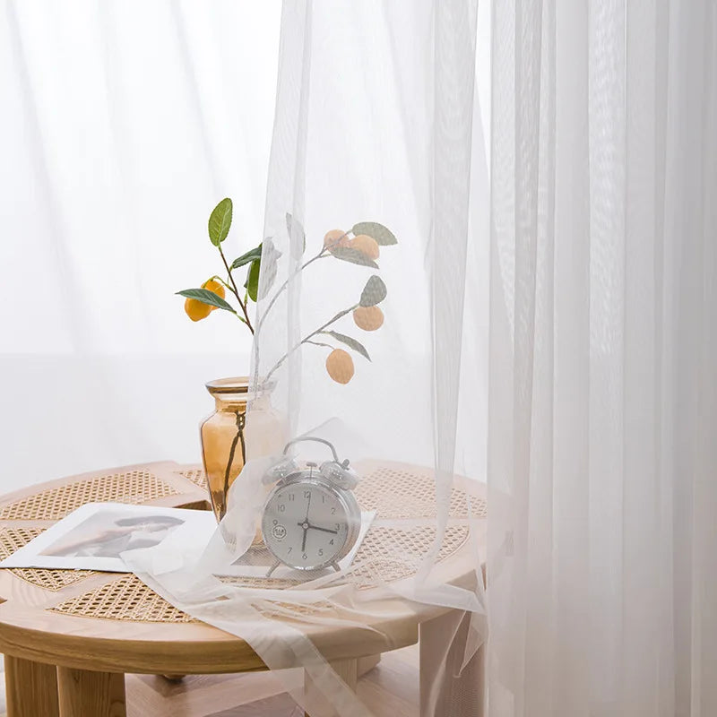 Semi-sheer white tulle curtains draped beside a wooden table with a vintage clock and olive branches.