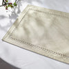 A rectangular beige linen placemat with delicate white geometric embroidery is displayed on a white surface.