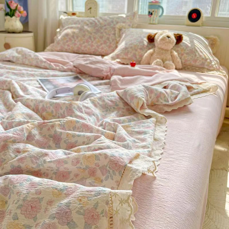 A pink quilt blanket with a floral print is displayed on a bed, next to pillows and a teddy bear.