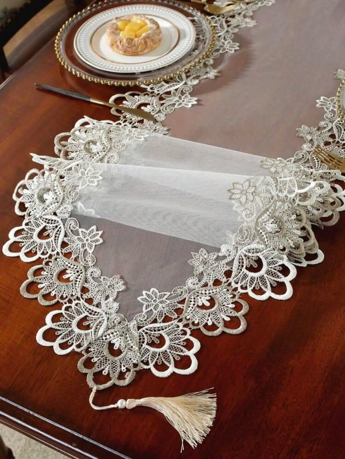 A white embroidered mesh lace table runner displayed on a dark wooden table.