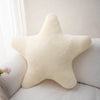 A cream-colored star-shaped plush throw pillow resting on a white surface.