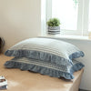 A set of two washed cotton pillowcases with a soft plaid pattern and ruffled edges displayed on a light wooden surface.