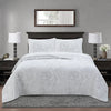 A white embroidered bedding set with a floral pattern displayed on a bed in a modern bedroom.