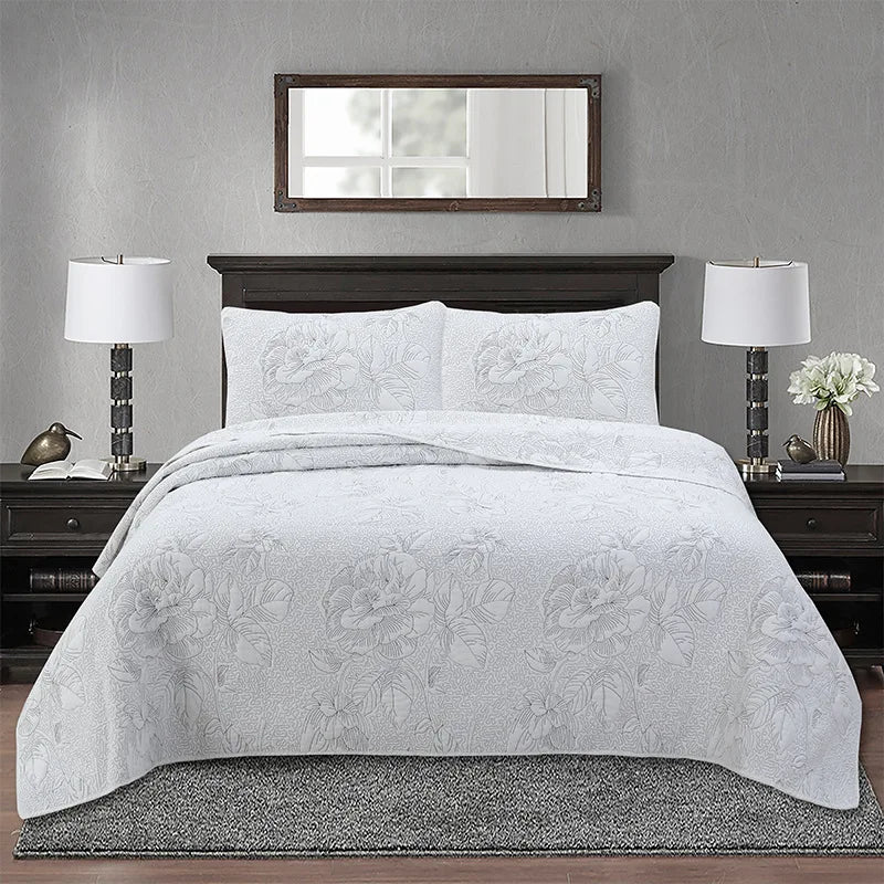 A white embroidered bedding set with a floral pattern displayed on a bed in a modern bedroom.