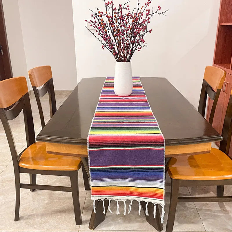 A dark wooden table set with a colorful cotton Mexican serape table runner and a vase of red berries.