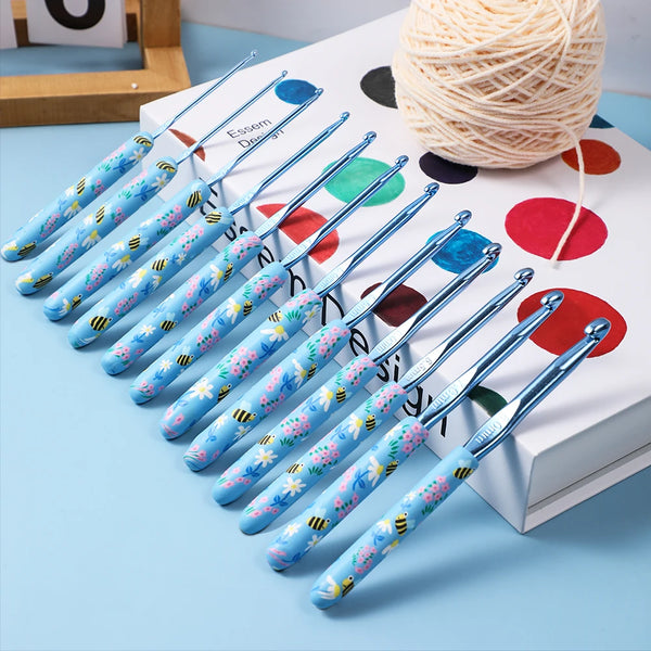 A set of blue and white ergonomic crochet hooks arranged diagonally on a light blue surface next to a white box.