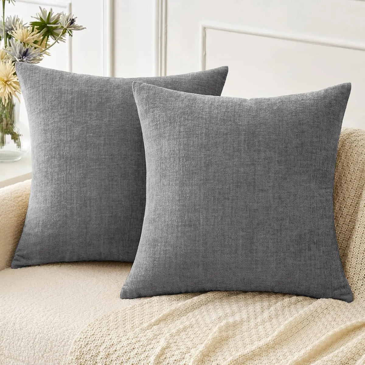 A solid gray chenille throw pillow cover resting on a light beige textured sofa.
