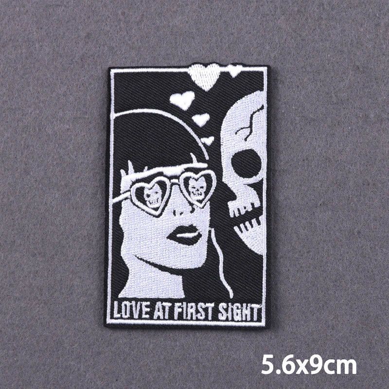 Black and white embroidered patch featuring a woman's face with heart-shaped glasses and a skull design.