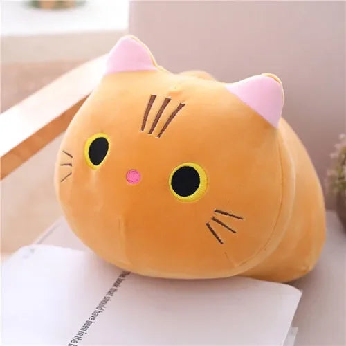 A soft orange cat plush pillow cushion with pink ears and yellow eyes resting on a white surface.