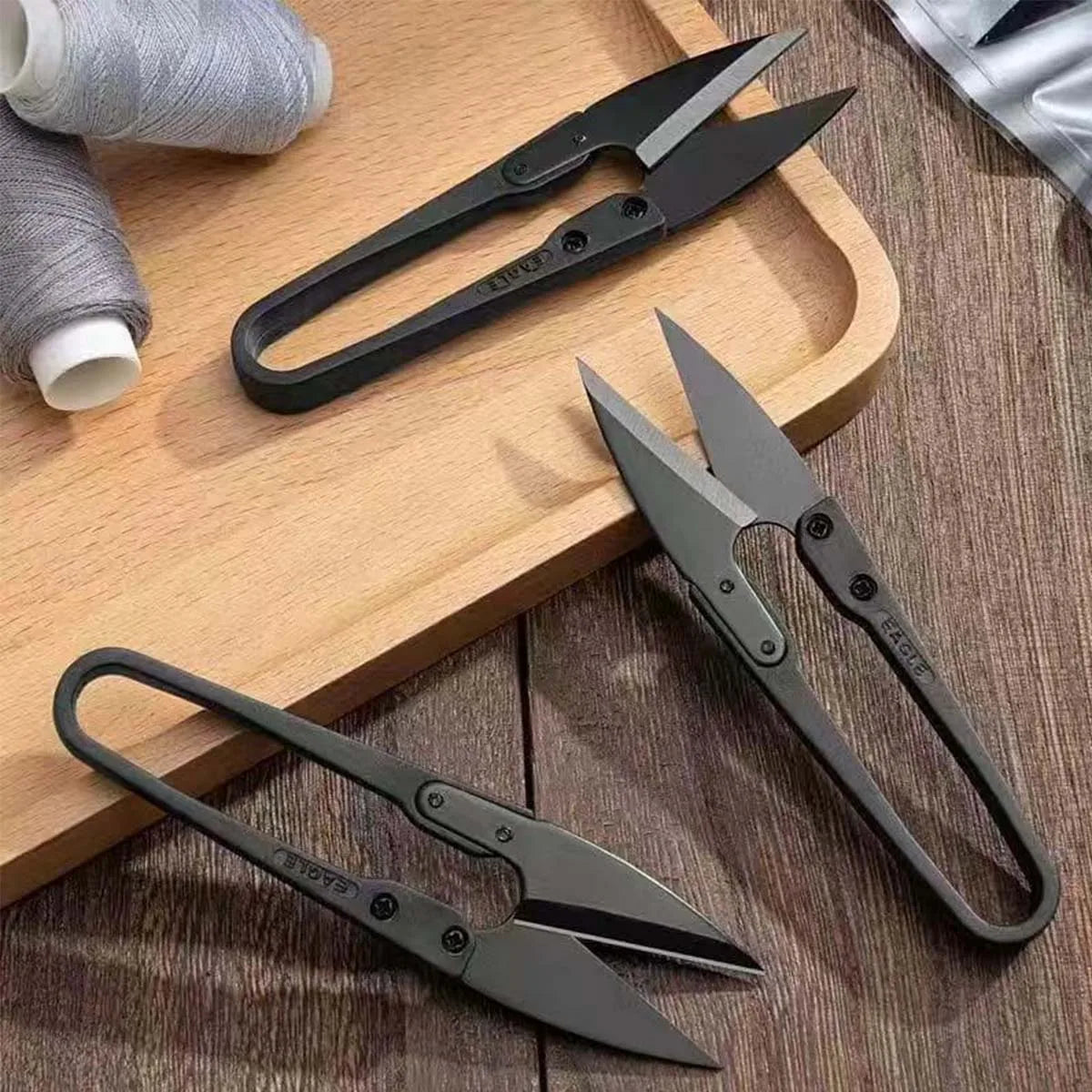 A set of ergonomic stainless steel thread snip scissors resting on a wooden surface.