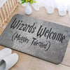 A gray entrance mat with the text Wizards Welcome Muggles Tolerated carved into it, placed on a wooden surface.