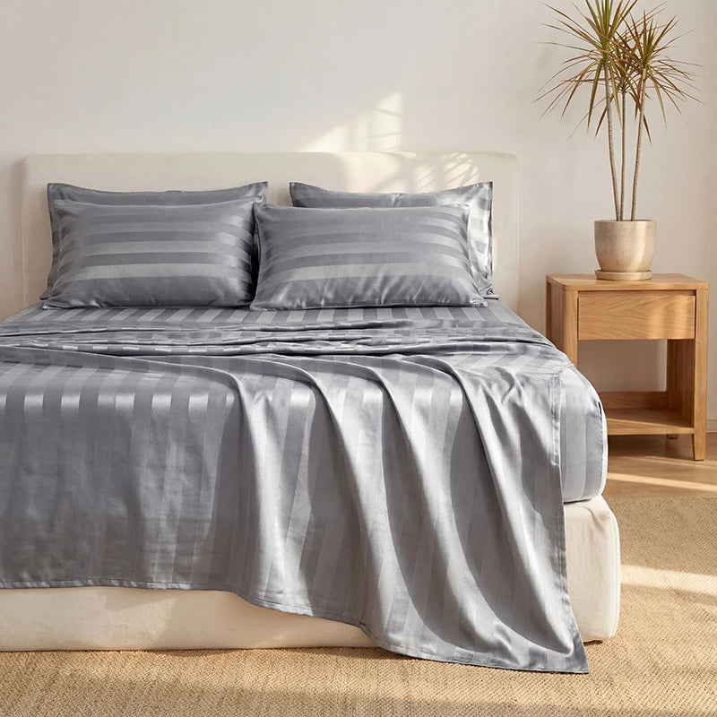 A gray wrinkle-resistant satin bedding set displayed on a bed with light wood furniture.