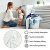A woman is using a laundry basket filled with a white, fluffy blanket near a washing machine.