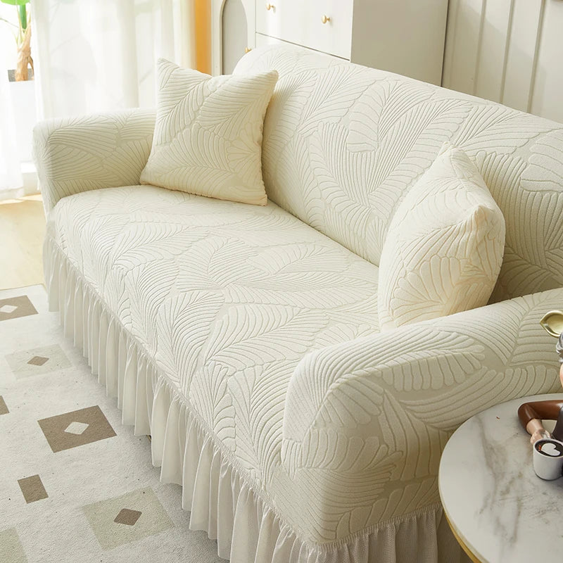 A cream jacquard elastic sofa cover with a pleated skirt shown on a light-colored sofa.