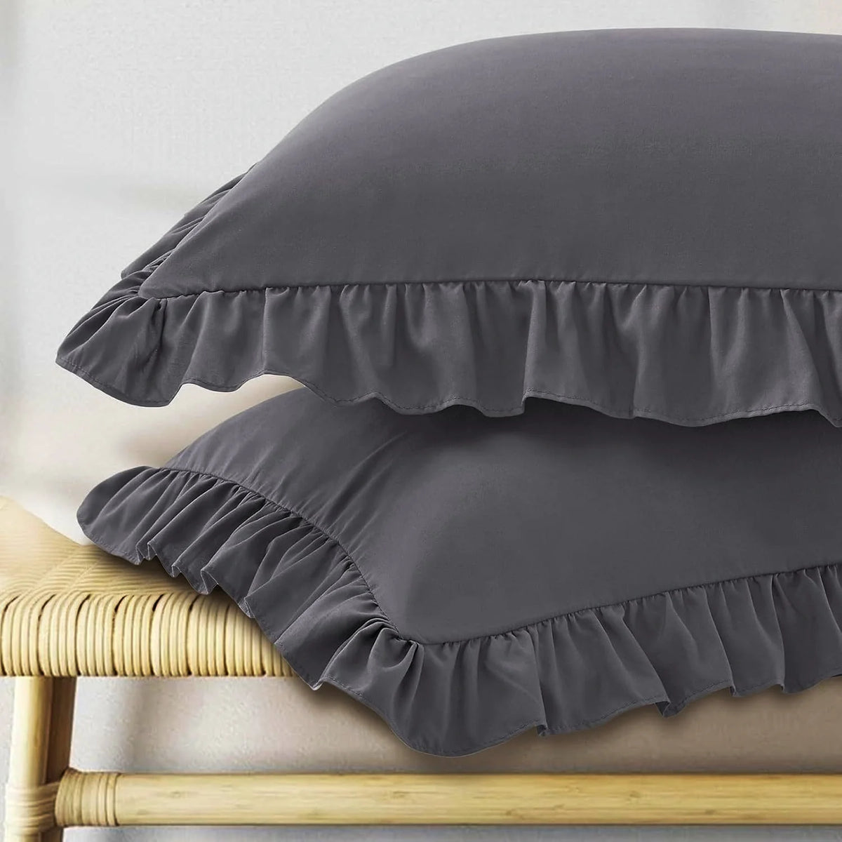 A set of two gray pillow covers with ruffled envelope closures resting on a light wooden surface.