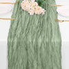 A sage green cheesecloth table runner with pink flowers and gold cutlery for rustic boho decor.