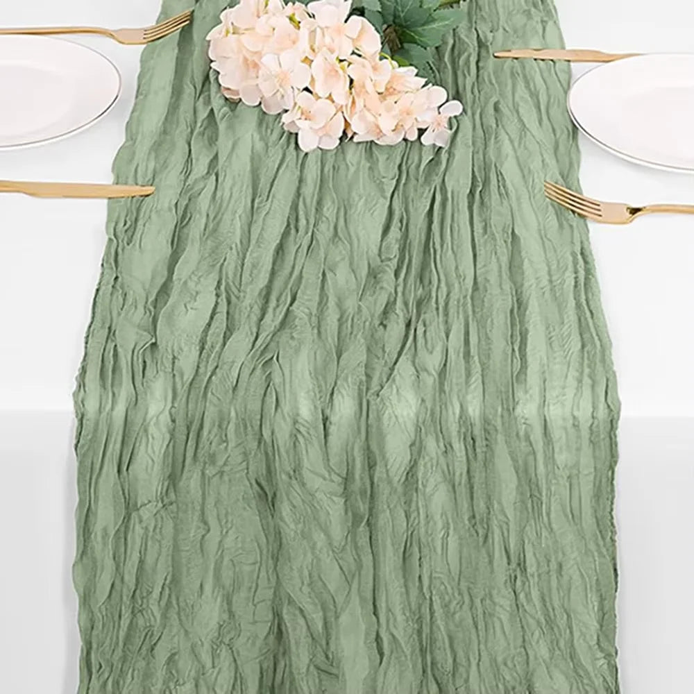 A sage green cheesecloth table runner with pink flowers and gold cutlery for rustic boho decor.