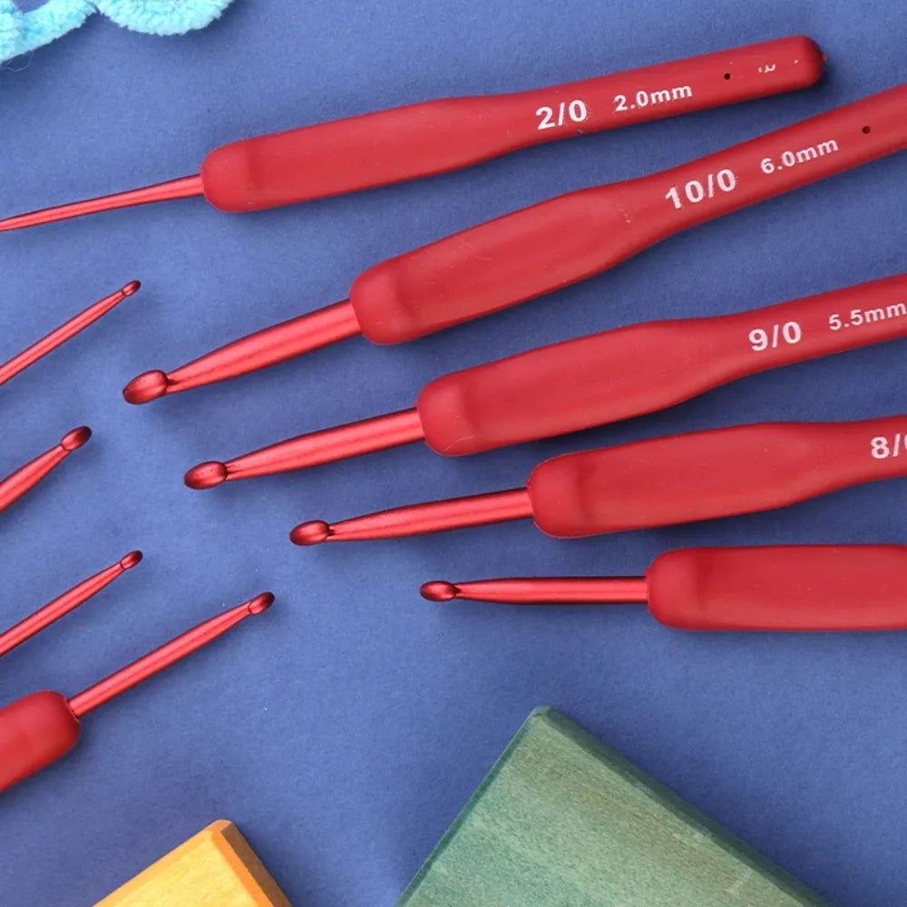 A collection of red ergonomic crochet hooks with various sizes and tips laid on a blue surface.
