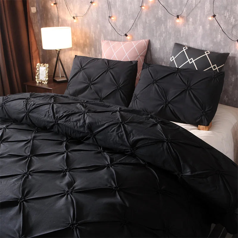 Black quilted duvet and pillows set against a gray wall with string lights.