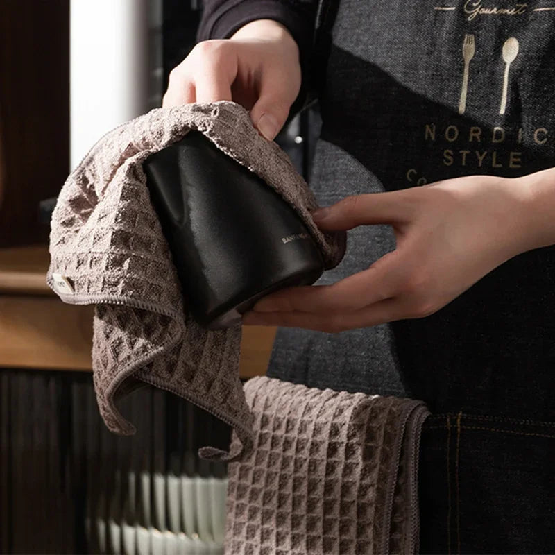 A hand is holding a dark cleaning towel wrapped around a black microfiber cloth for coffee machine use.