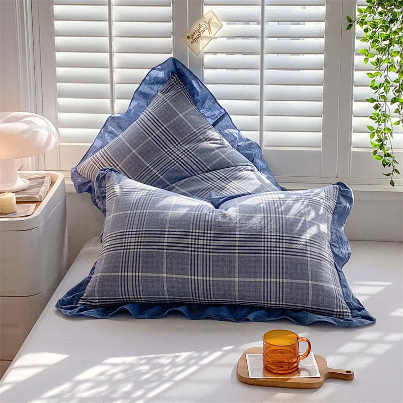 Two blue and gray plaid washed cotton pillowcases with ruffled edges resting on a white surface.