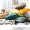 A collection of various colored velvet cushions, including gray, yellow, and teal, displayed on a light-colored sofa.