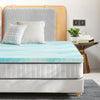 A light blue cooling memory foam mattress topper placed on a bed with neutral bedding and wooden headboard.
