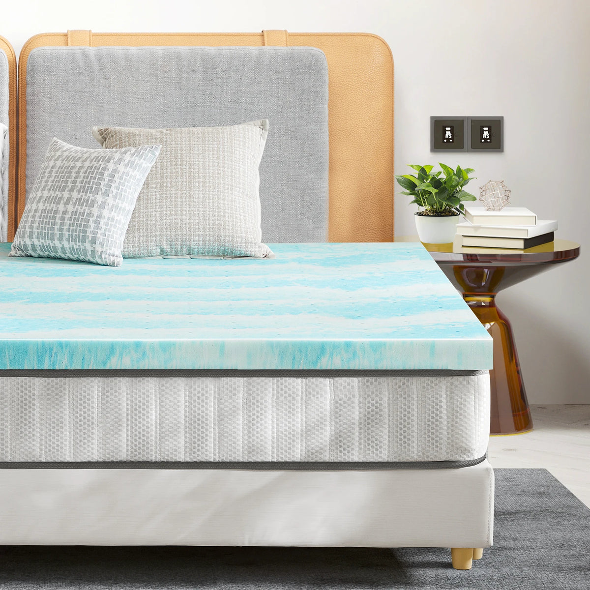 A light blue cooling memory foam mattress topper placed on a bed with neutral bedding and wooden headboard.
