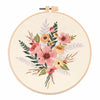 A round embroidery hoop featuring a floral pattern of pink, yellow, and green foliage on a cream fabric.