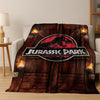 A dark brown flannel throw blanket featuring a Jurassic Park dinosaur graphic on a wooden background.