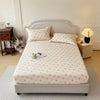 A floral printed cotton fitted sheet displayed on a bed with a light gray upholstered headboard and bedside lamp.