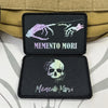 Two black embroidered badge patches featuring a purple insect and a skull design on a tan tactical strap.