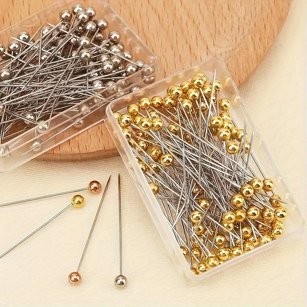 A clear plastic container holds various precision positioning pins in silver and gold colors.