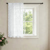 White vintage French-style lace curtain hanging in a window on a light wall.
