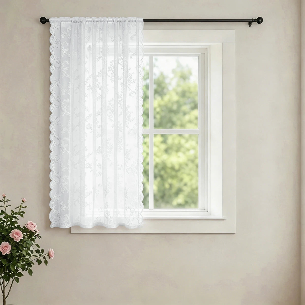 White vintage French-style lace curtain hanging in a window on a light wall.