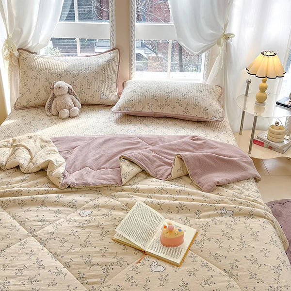 A light beige cartoon quilting comforter spread on a bed with white curtains and pillows.