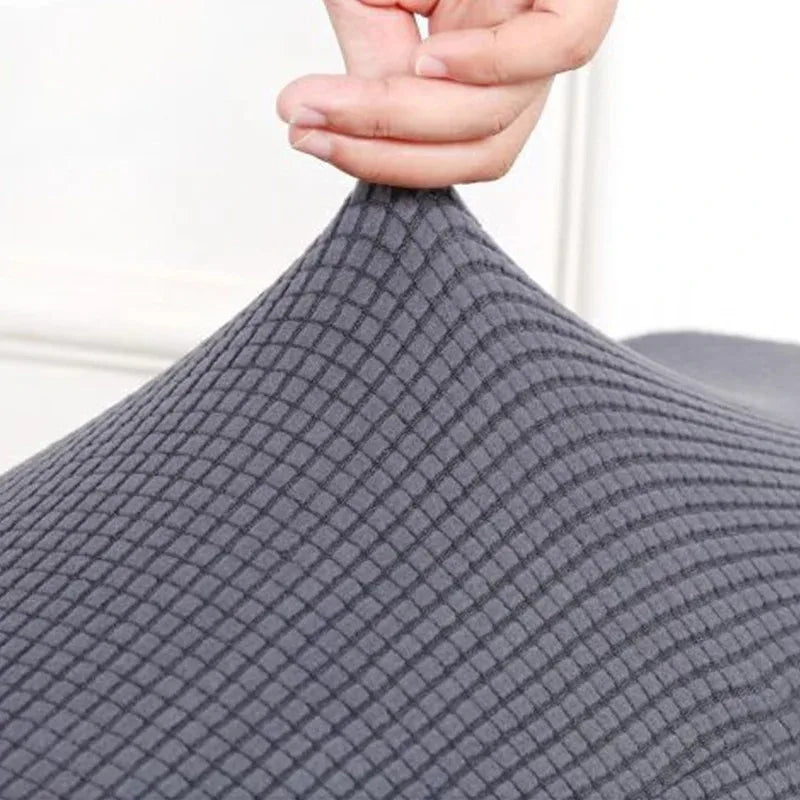 A hand is adjusting the fabric of a gray, textured elastic stool cover for living room seating.