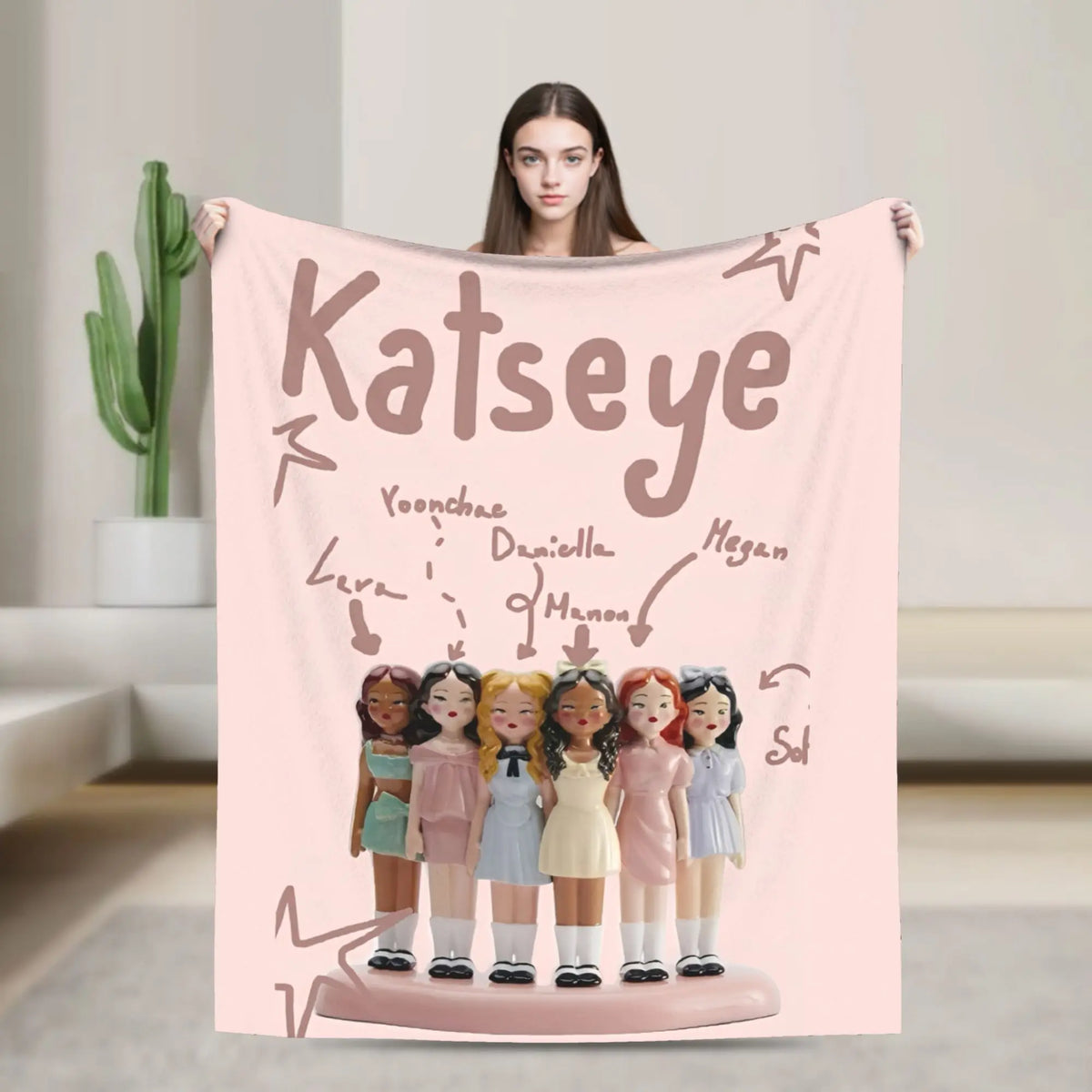 A pink fleece throw blanket featuring illustrations of K-Pop idols and the name Katseye.