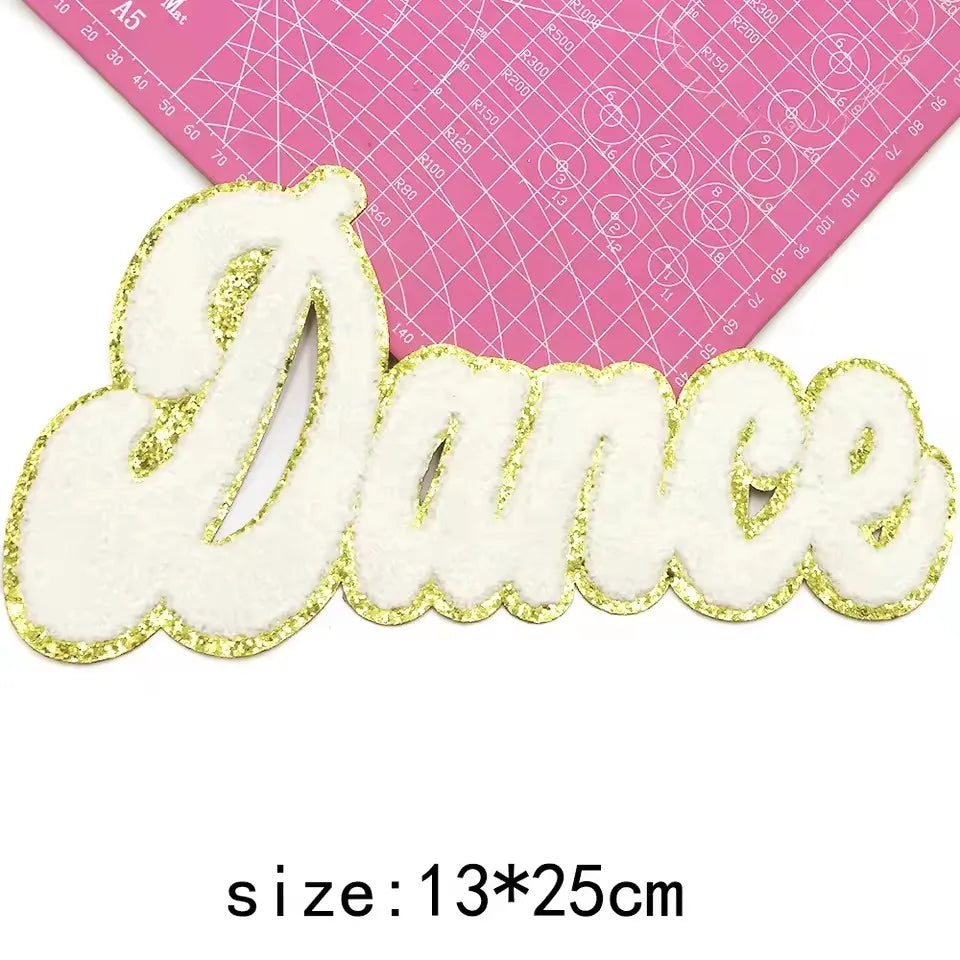 Gold glitter embroidered cheer letter patch spelling the word Dance on a pink grid background
