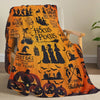 An orange and black Halloween-themed flannel throw blanket featuring witches, pumpkins, and spooky designs.