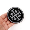 Black embroidered military cross shield hook and loop patch held in a hand