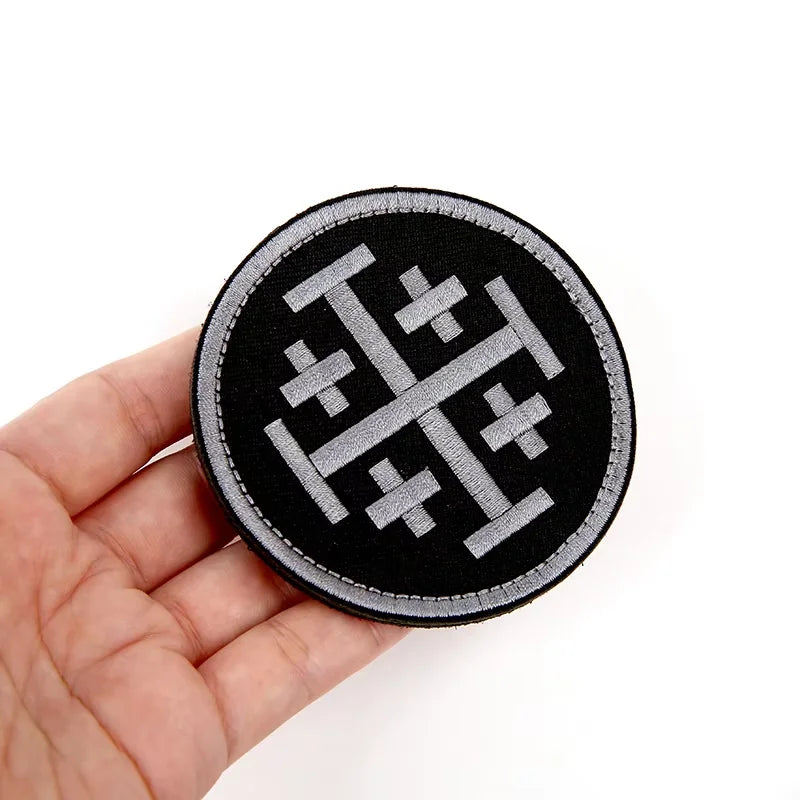 Black embroidered military cross shield hook and loop patch held in a hand