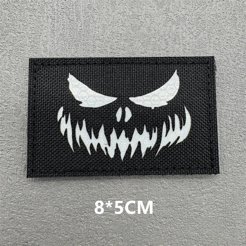 Black embroidered patch featuring a white demonic face design on a gray fabric background
