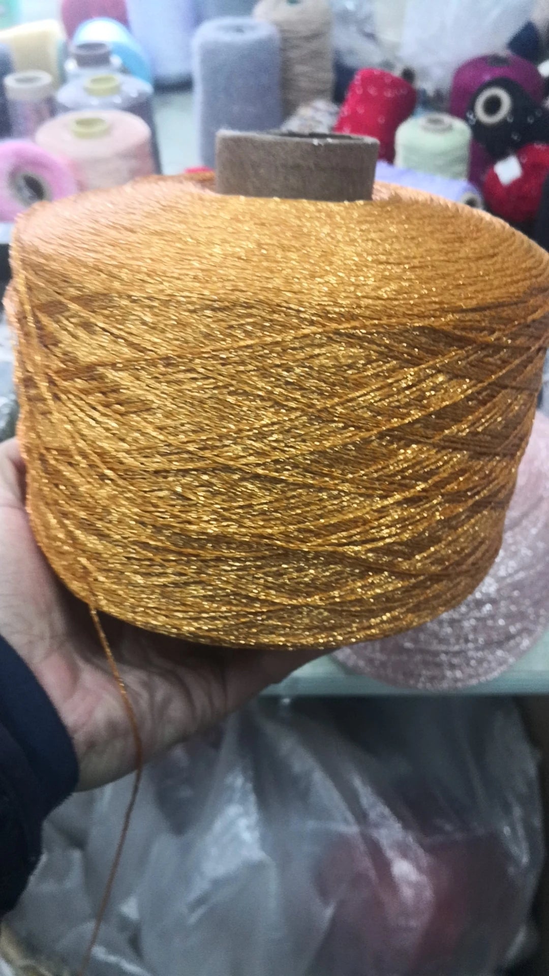 A hand holds a spool of metallic gold glitter yarn for crochet and knitting.
