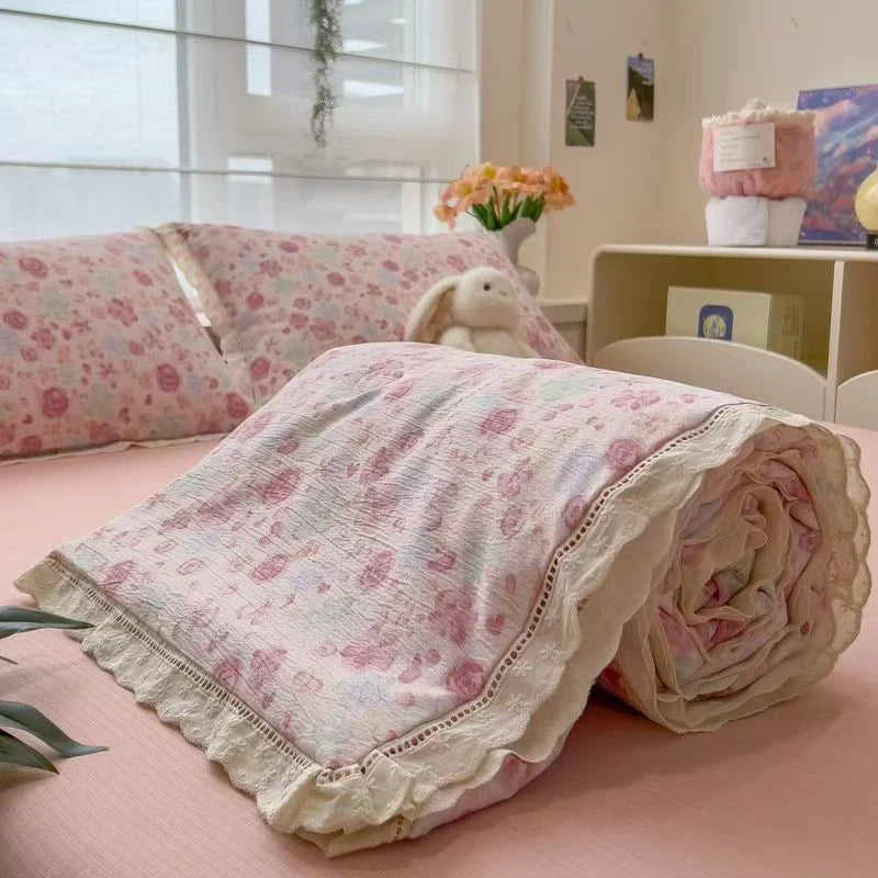 A pink quilt blanket with a floral print is rolled up on a light pink bed.