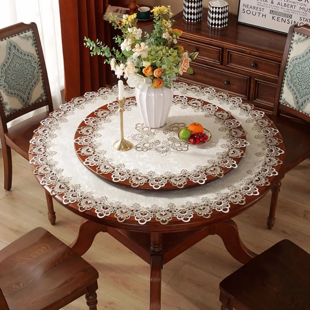 An elegant lace-trimmed round tablecloth set on a wooden table with floral arrangements and decorative boxes.