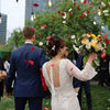 A bride in a white dress is tossing red and white silk rose petals outdoors during her wedding ceremony.