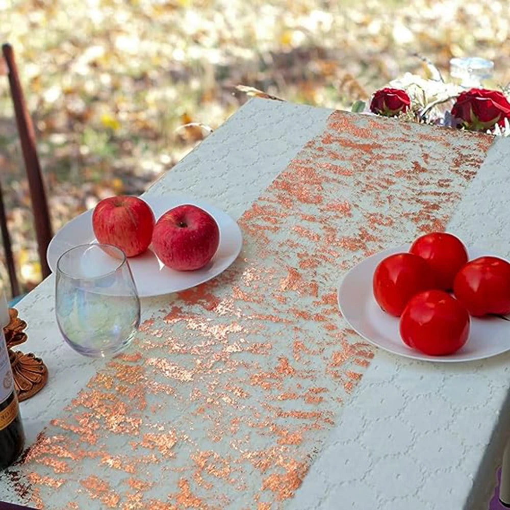 A white table is decorated with an orange sequin glitter runner, red apples, and a glass on an outdoor setting.