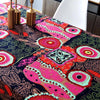 Close-up of a table covered with a vibrant bohemian printed linen fabric featuring pink, orange, and teal patterns.