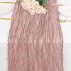 A dusty rose burgundy cheesecloth table runner with white flowers and gold cutlery.